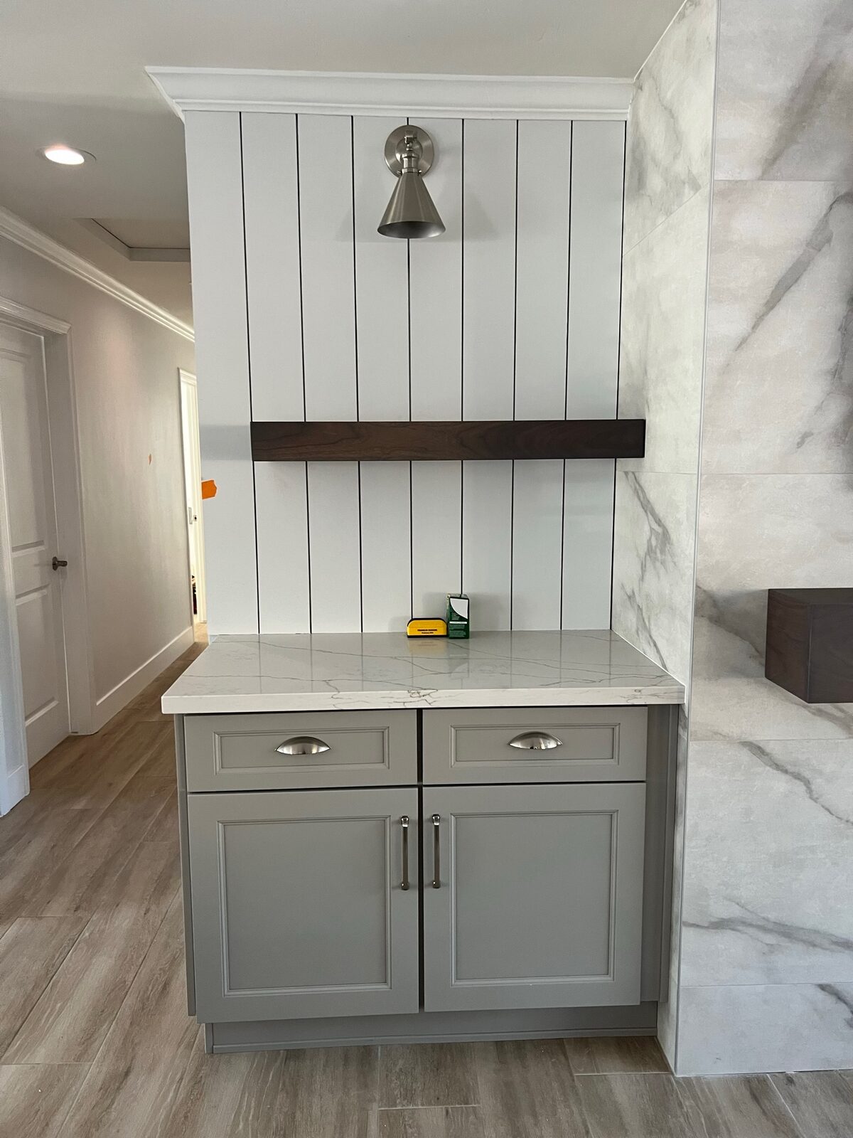 Gray base cabinet with quartz top, vertical plank wall, wood shelf and metal sconce