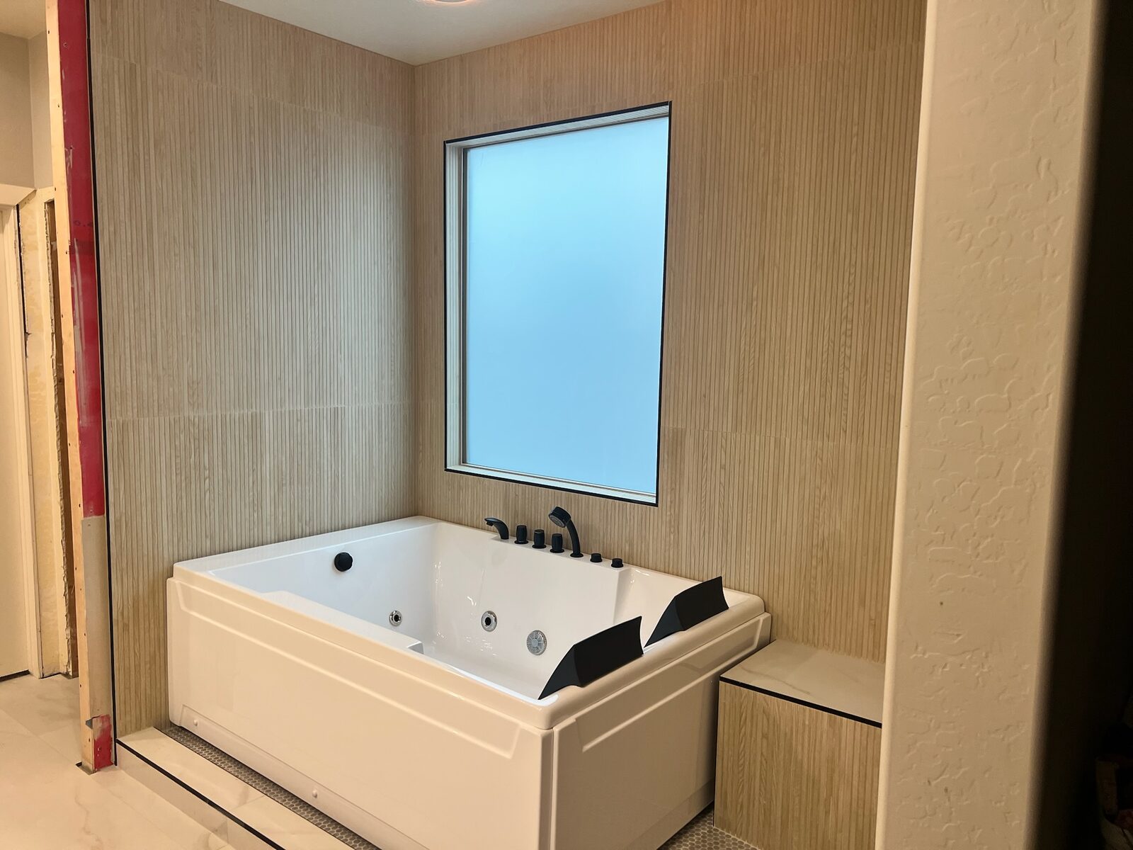Jetted soaking tub with black fixtures installed against fluted tile walls under a frosted window