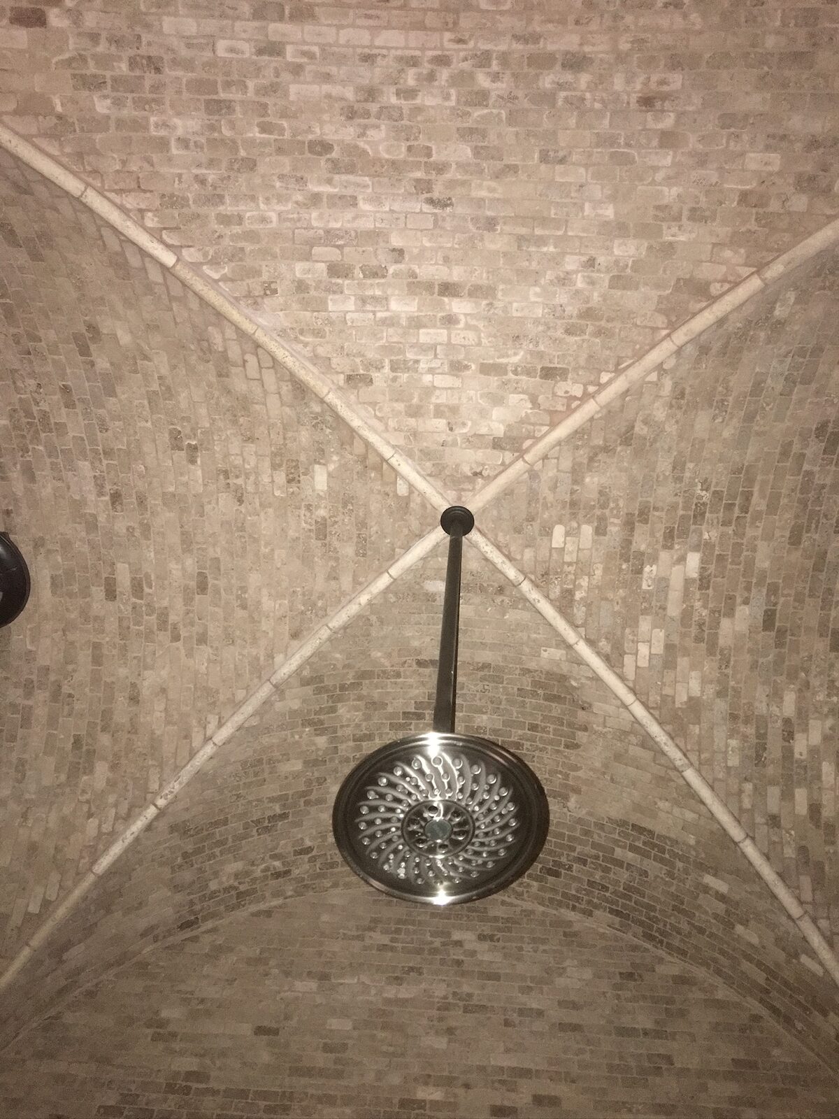 Rain shower head centered under a groin vault ceiling tiled in stone mosaic