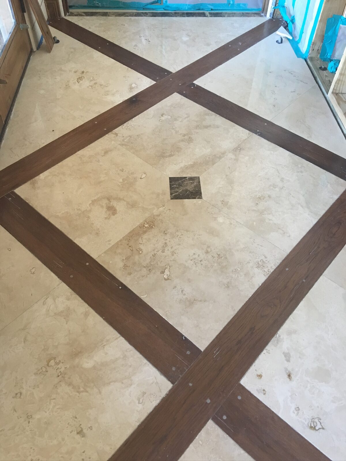 Travertine floor with dark wood inlay strips in a diamond pattern and a marble center accent